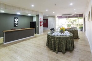 A spacious room with a reception desk, a round table with a patterned tablecloth, and a wall-mounted fire extinguisher. - Hotel Vila Rica Campinas (Campinas)