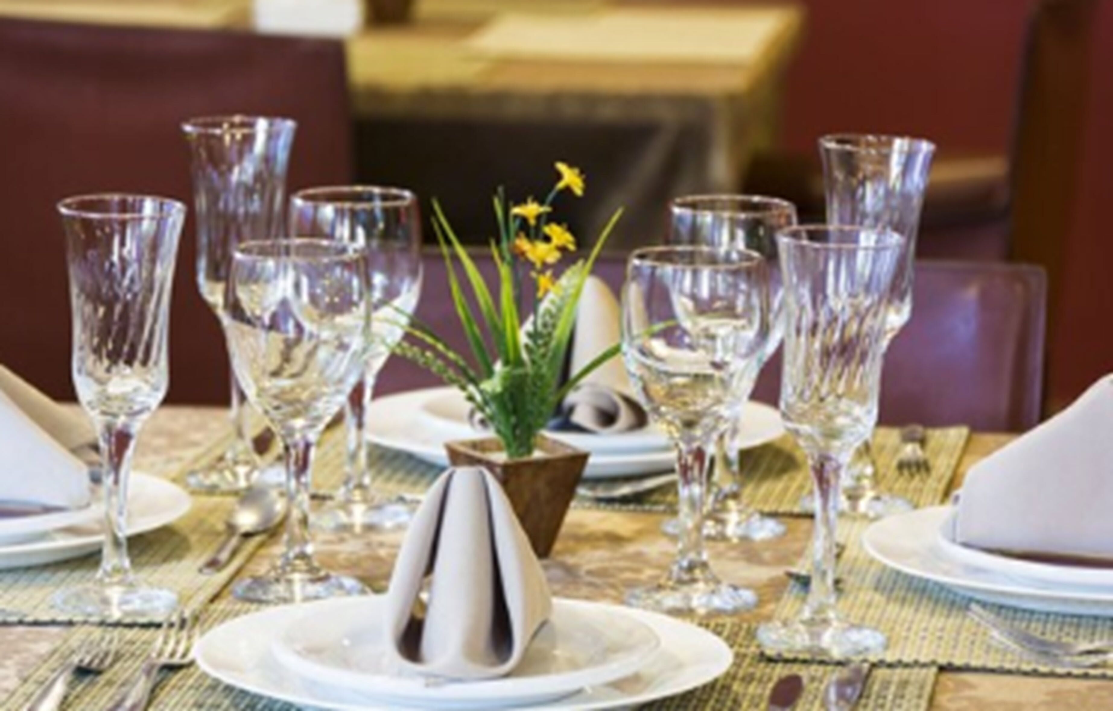 A dining table set with multiple wine glasses, plates, and a centerpiece with flowers.