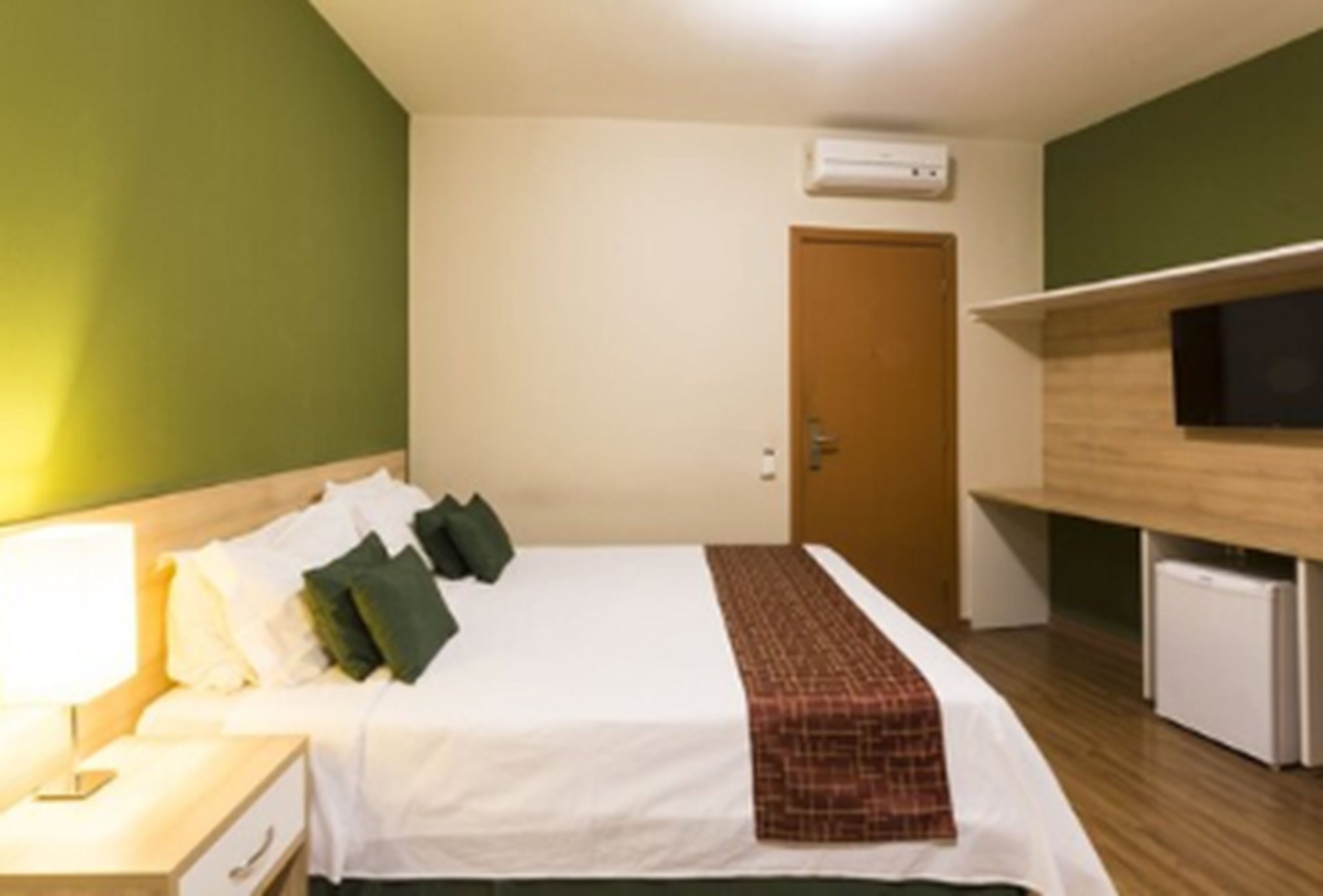 Una camera d'albergo con un letto, un comodino, una lampada e un televisore su un ripiano.