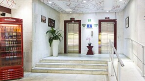 Un hall de hotel con una máquina expendedora, una planta en maceta y una escalera que lleva a los ascensores.