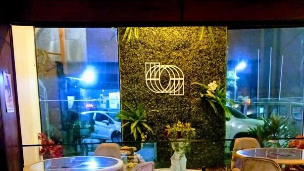 Un interior de restaurante con mesas y sillas redondas, una pared decorativa con un logotipo y vista a la calle.