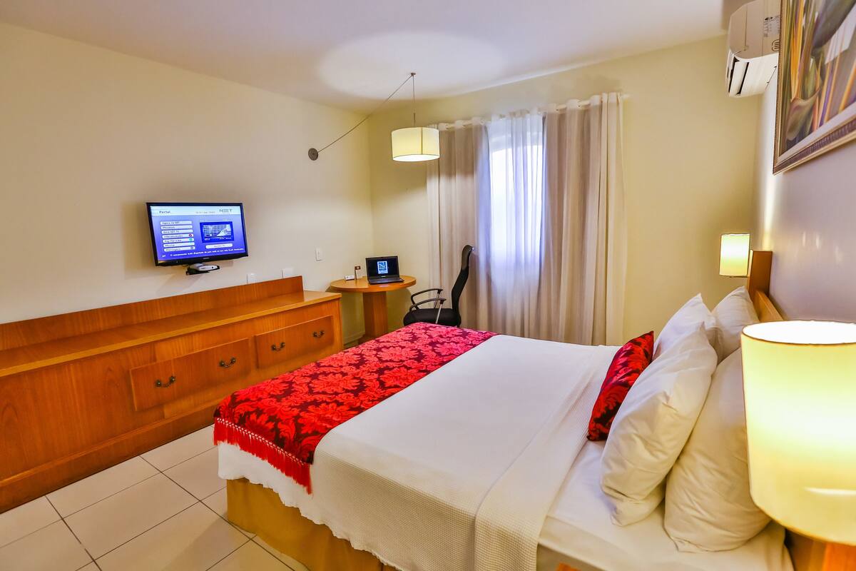 A hotel room with a bed, a desk, a chair, a television, and a window with curtains.