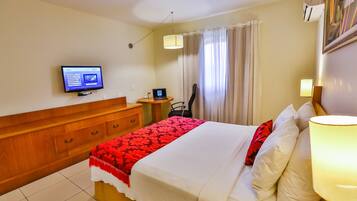 A hotel room with a bed, a desk, a chair, a television, and a window with curtains.