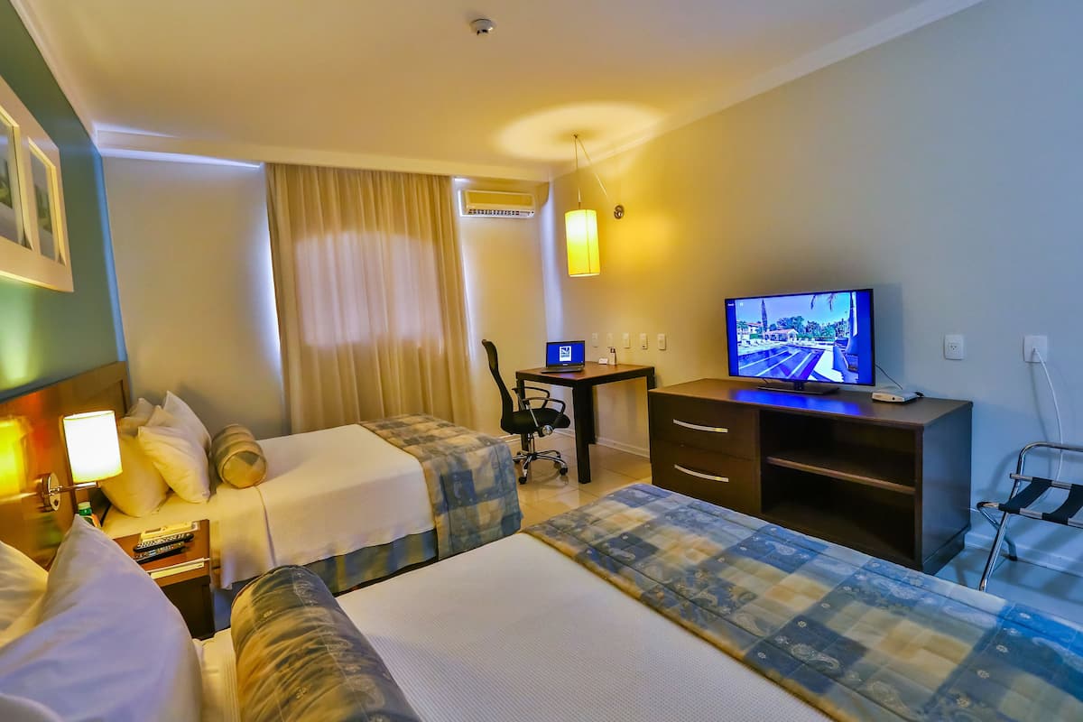 A hotel room with two beds, a desk with a computer, a TV, and a chair.