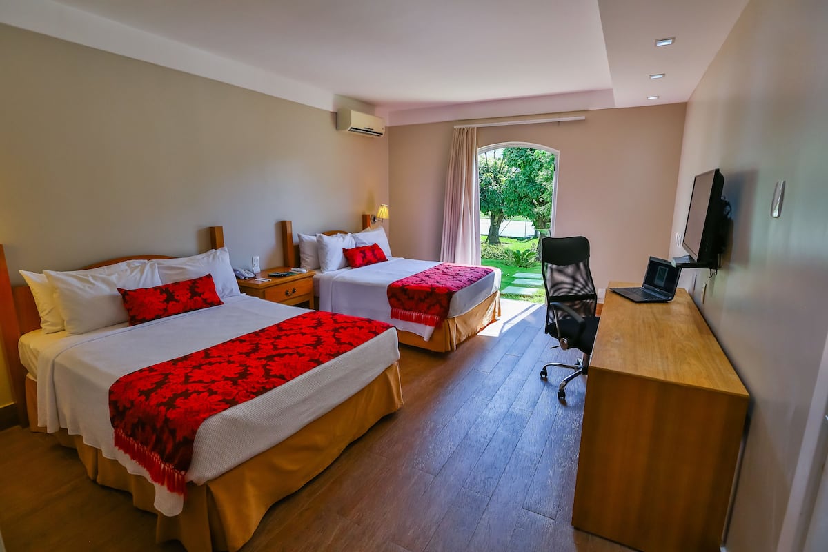 A hotel room with two beds, a desk, a chair, and a TV.