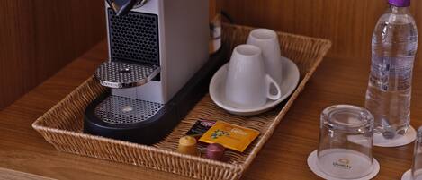 A coffee machine on a tray with two white cups, a water bottle, and a small card.