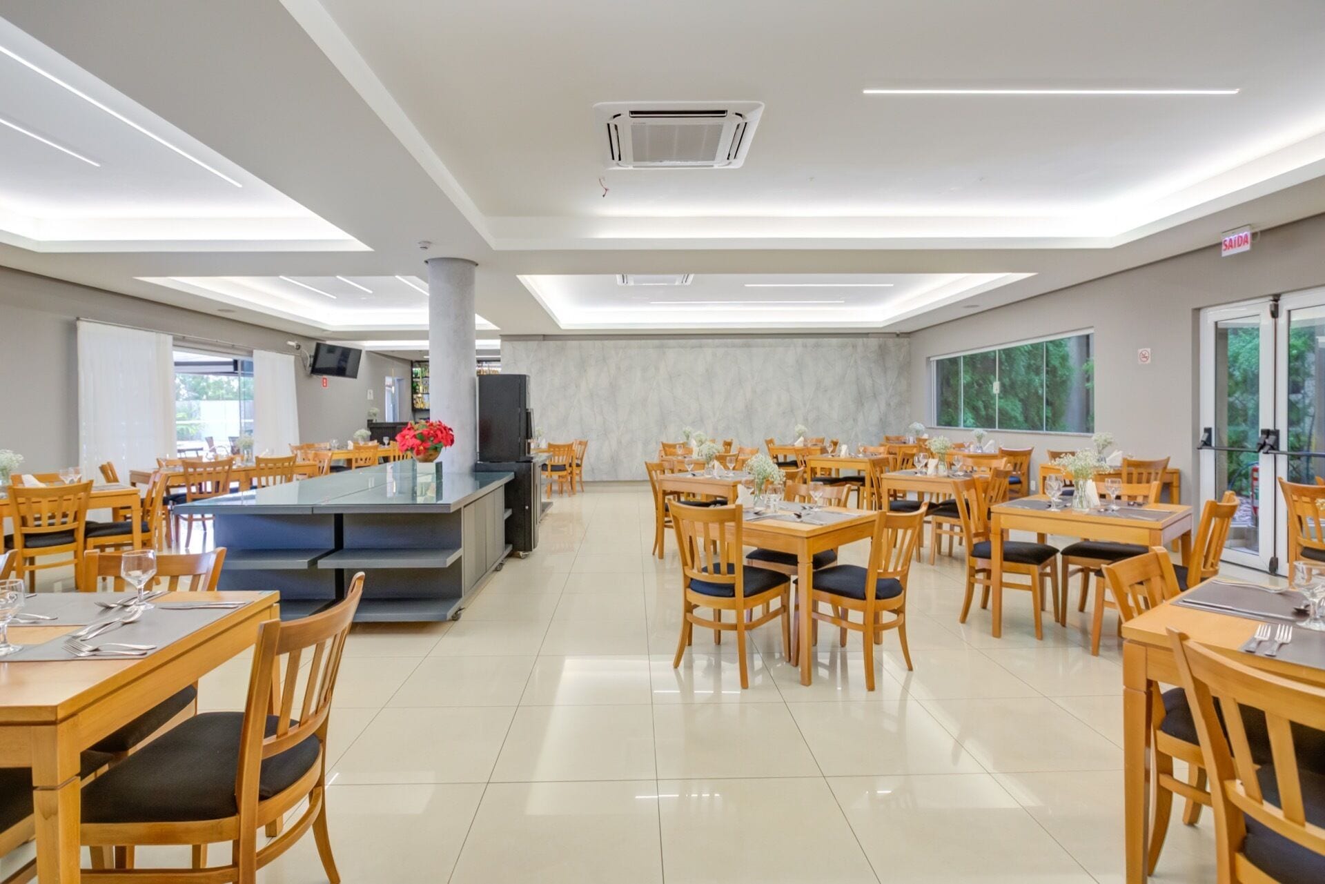 A spacious dining area with multiple tables and chairs, a central bar, and a large window providing natural light.