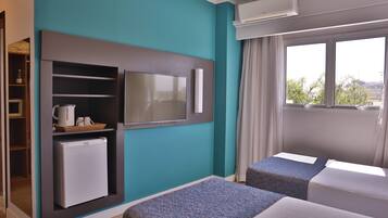 A hotel room with teal walls, a TV mounted on the wall, a mini-fridge, a microwave, a window with curtains, and two beds.