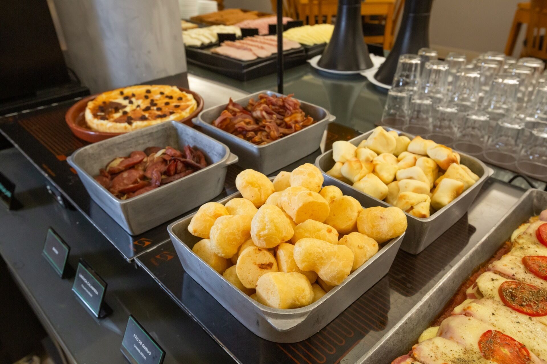 Buffet com diversos itens de comida, incluindo pães, carnes e pizza.