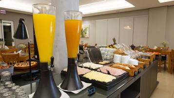 A buffet area with juice dispensers, a waffle maker, and various food items.