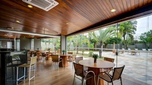 Un comedor interior moderno con piso de madera, mesas redondas y sillas de mimbre.