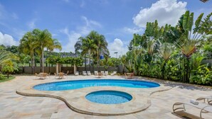Una piscina con un jacuzzi circular, rodeada de sillas de descanso y palmeras.