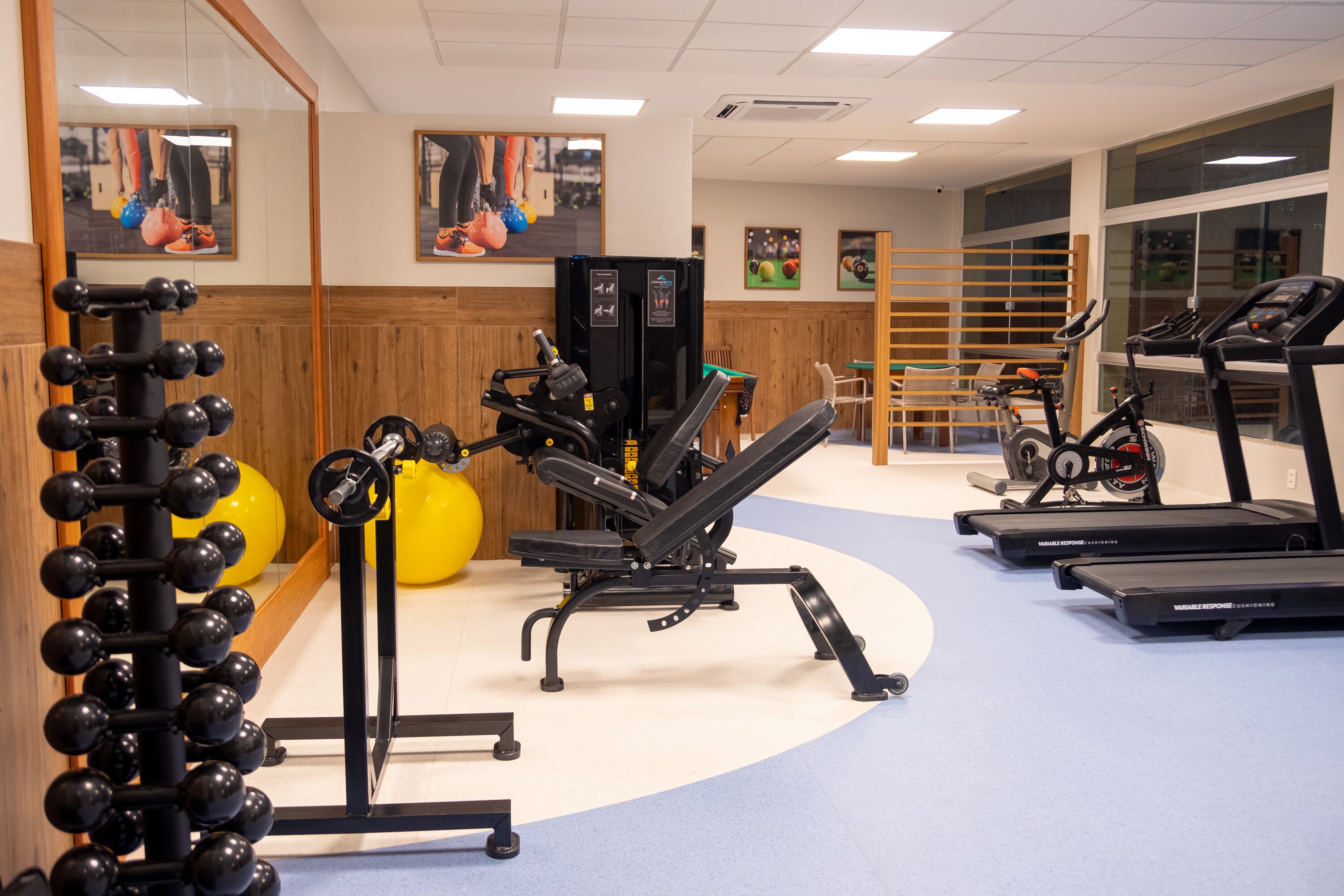 Ein Fitnessraum mit Trainingsgeräten, darunter Laufbänder, eine Hantelbank und ein Squat-Gestell.