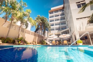 Una piscina con pavimento piastrellato, circondata da lettini e ombrelloni.