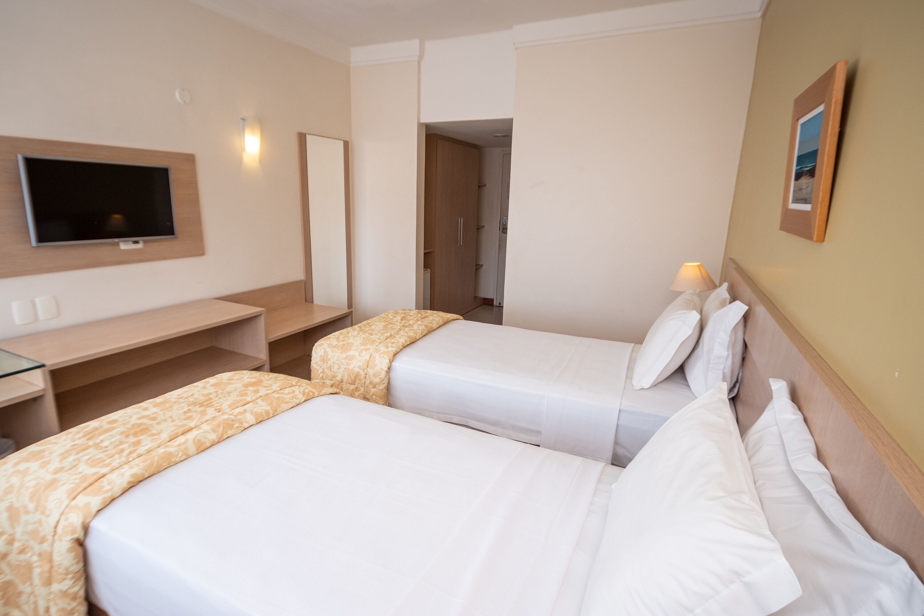 Une chambre d’hôtel avec deux lits, un bureau, une télévision et une porte donnant sur une autre chambre.