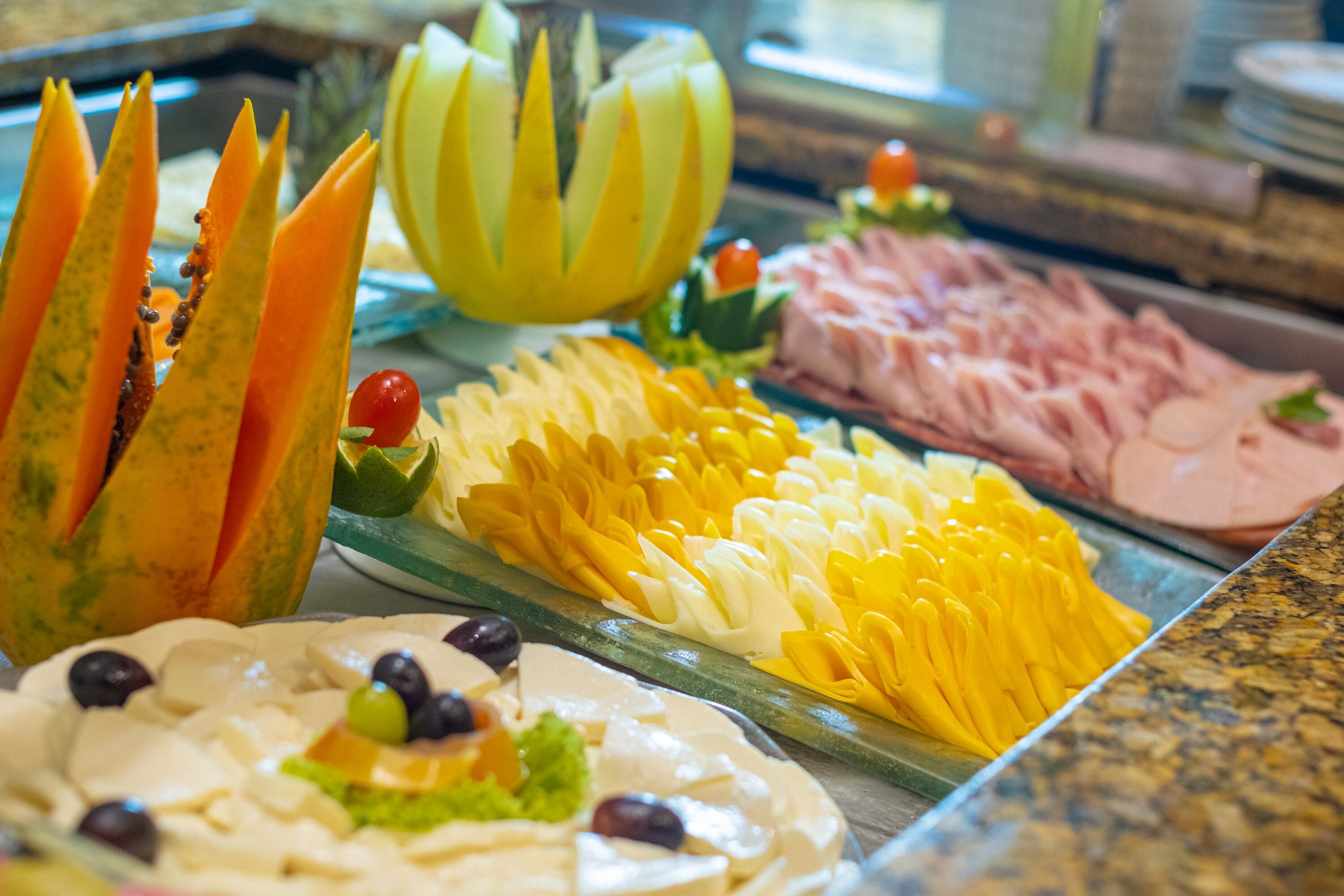 Un bufé con diversas opciones de comida, entre ellas frutas cortadas, verduras y carnes.
