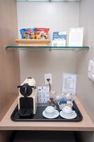 A kitchenette with a coffee machine, tea pots, and snack packets on a tray.
