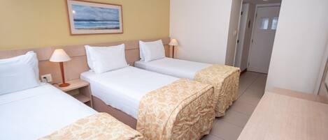 A hotel room with two beds, a desk, and a chair. There is a painting on the wall and a door in the background.