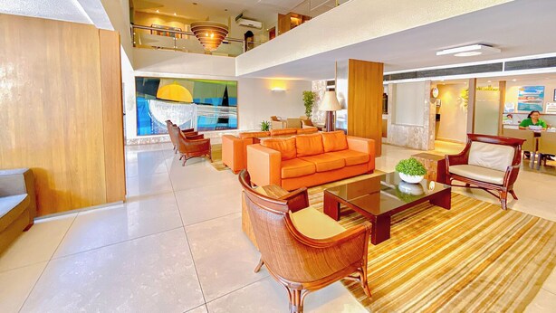 Un vestíbulo amplio con un sofá moderno color naranja, sillas de madera y una mesa de centro de vidrio.
