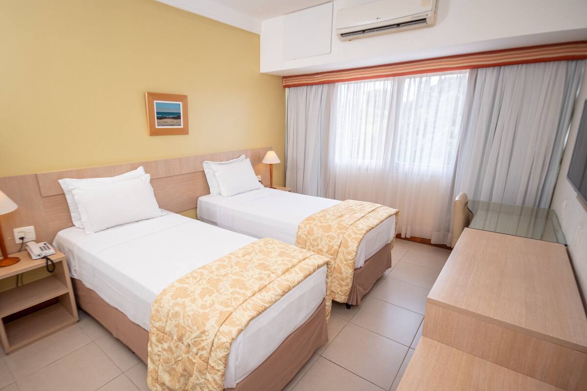 A hotel room with two beds, a desk, a chair, a phone, and a picture on the wall.