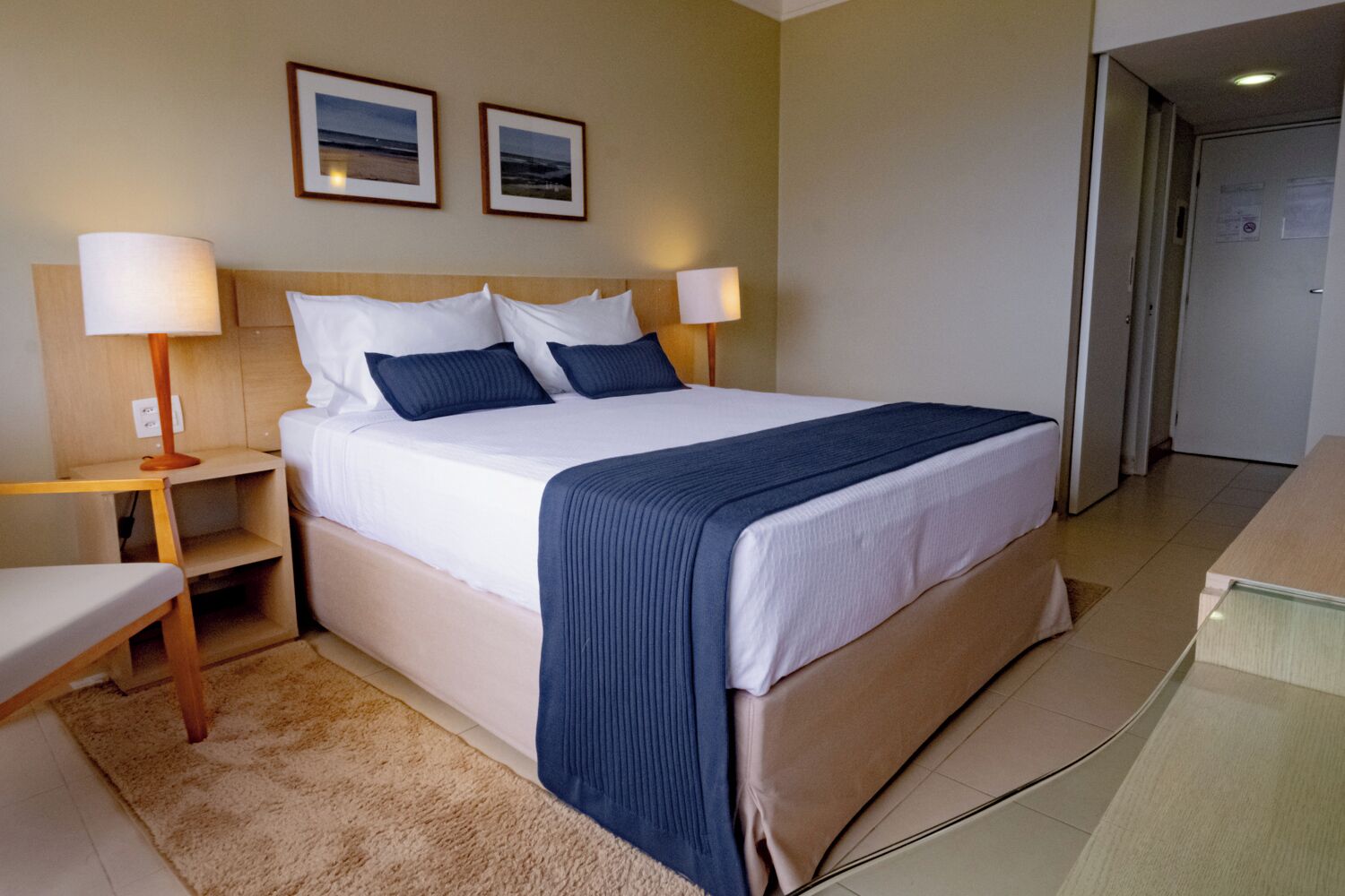Une chambre d’hôtel bien rangée, avec un lit, des tables de chevet, une chaise et une porte.