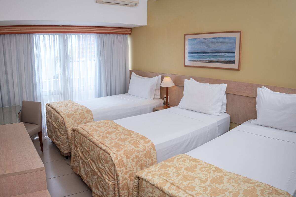 A hotel room with two beds, a TV, a desk, and a painting of a beach.