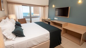 Habitación de hotel con cama, escritorio, silla, televisor y vista al océano.