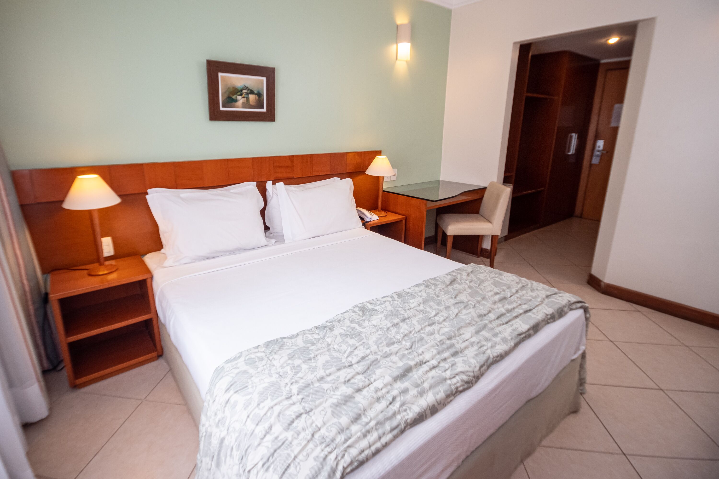Une chambre d’hôtel avec un lit, des lampes de chevet, un bureau et une chaise.