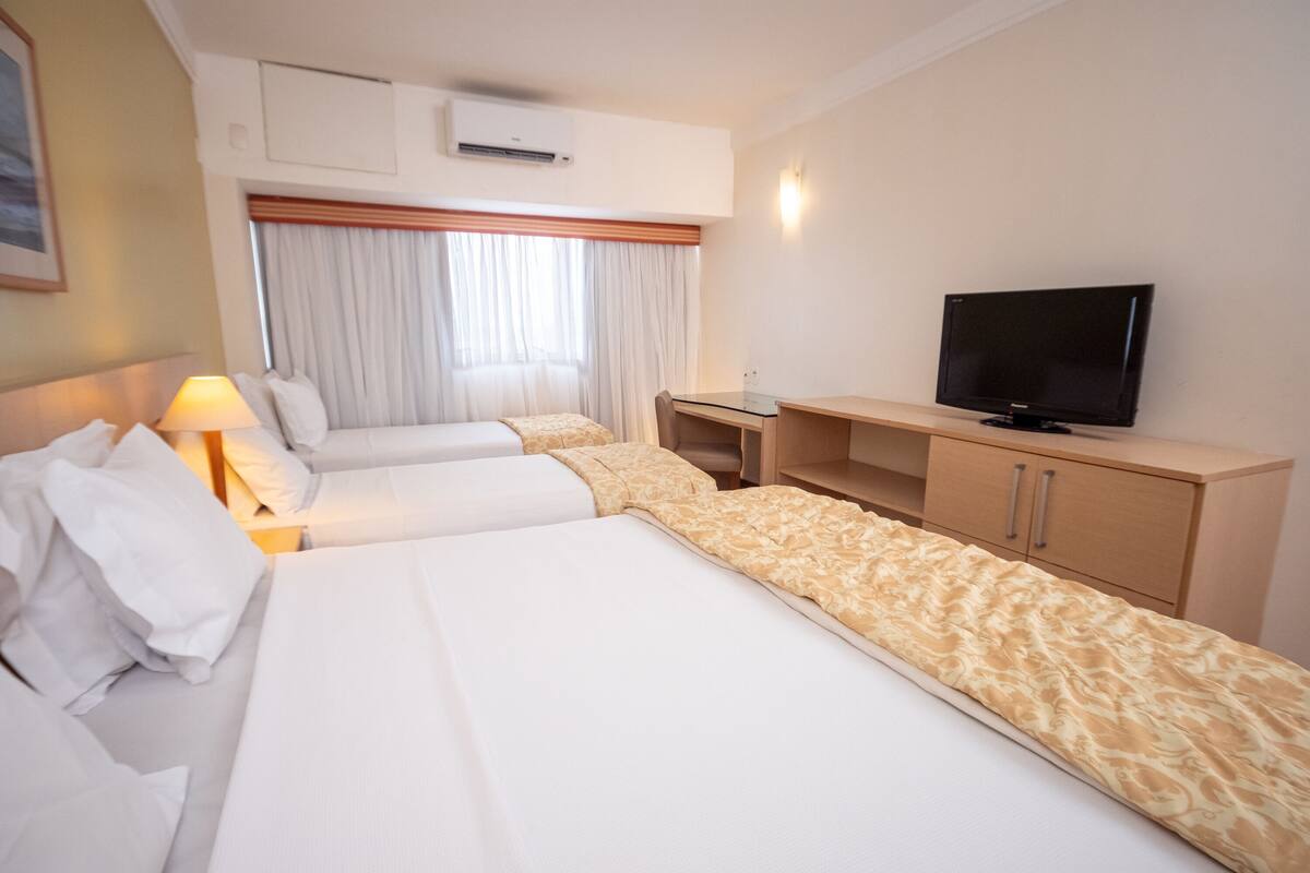 A hotel room with two beds, a television, a desk, and a window with curtains.
