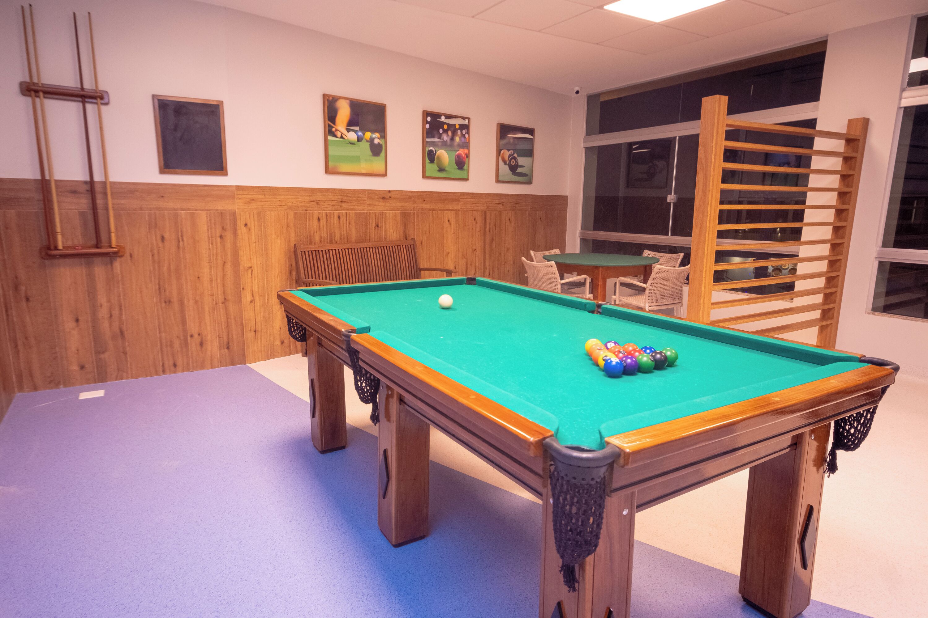 A pool table with a green felt surface, surrounded by wooden furniture and a wooden wall panel.