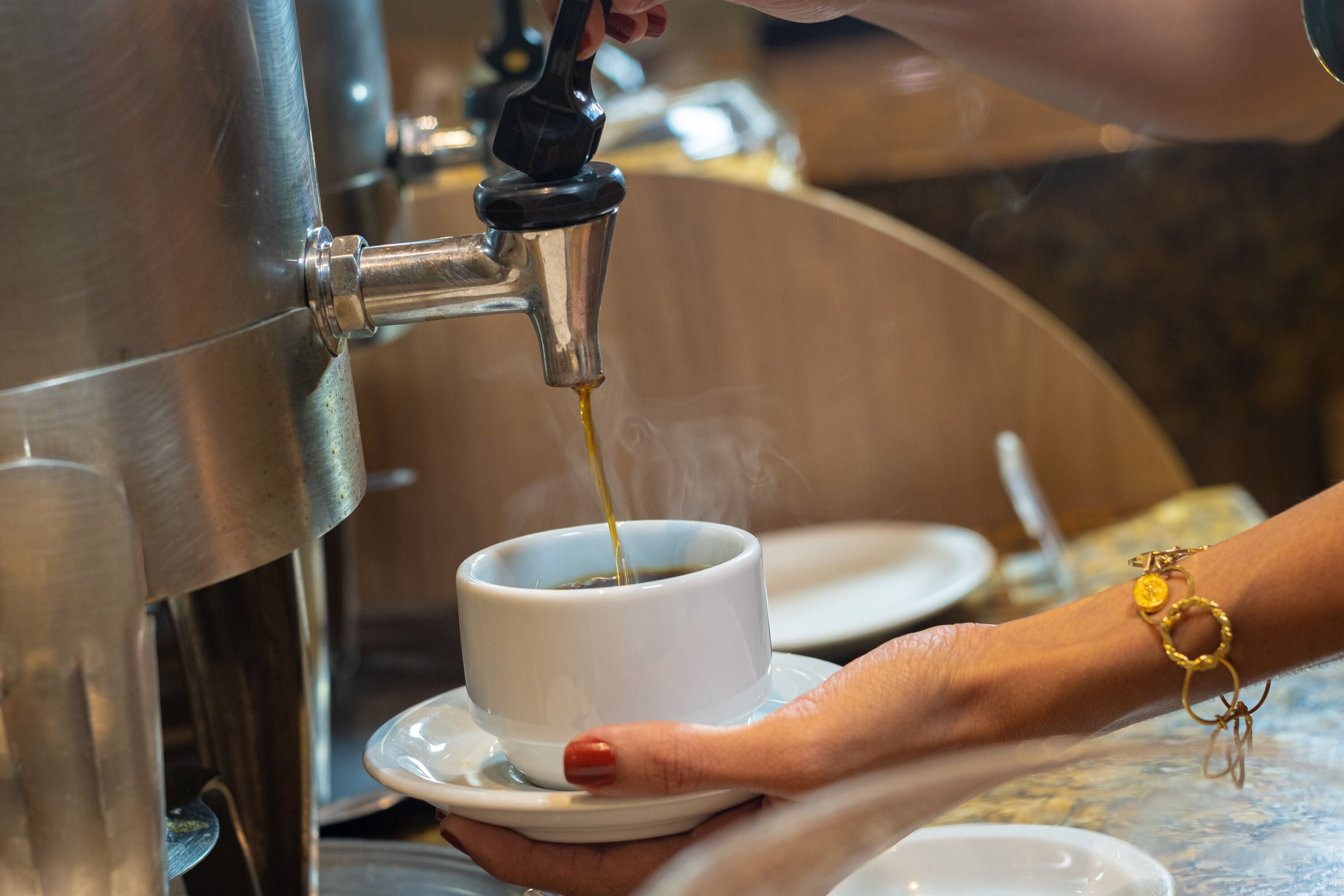 A hand holding a cup under a coffee machine, with steam rising from the cup.