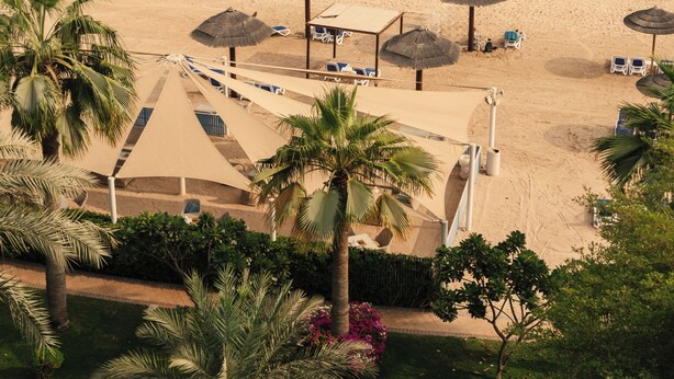 Een strandresort met parasols, ligbedden en palmbomen.