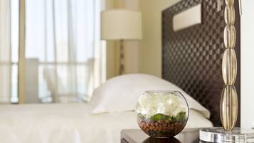 Habitación de hotel con cama, lámpara de noche y un cuenco decorativo con flores y nueces sobre la mesita.