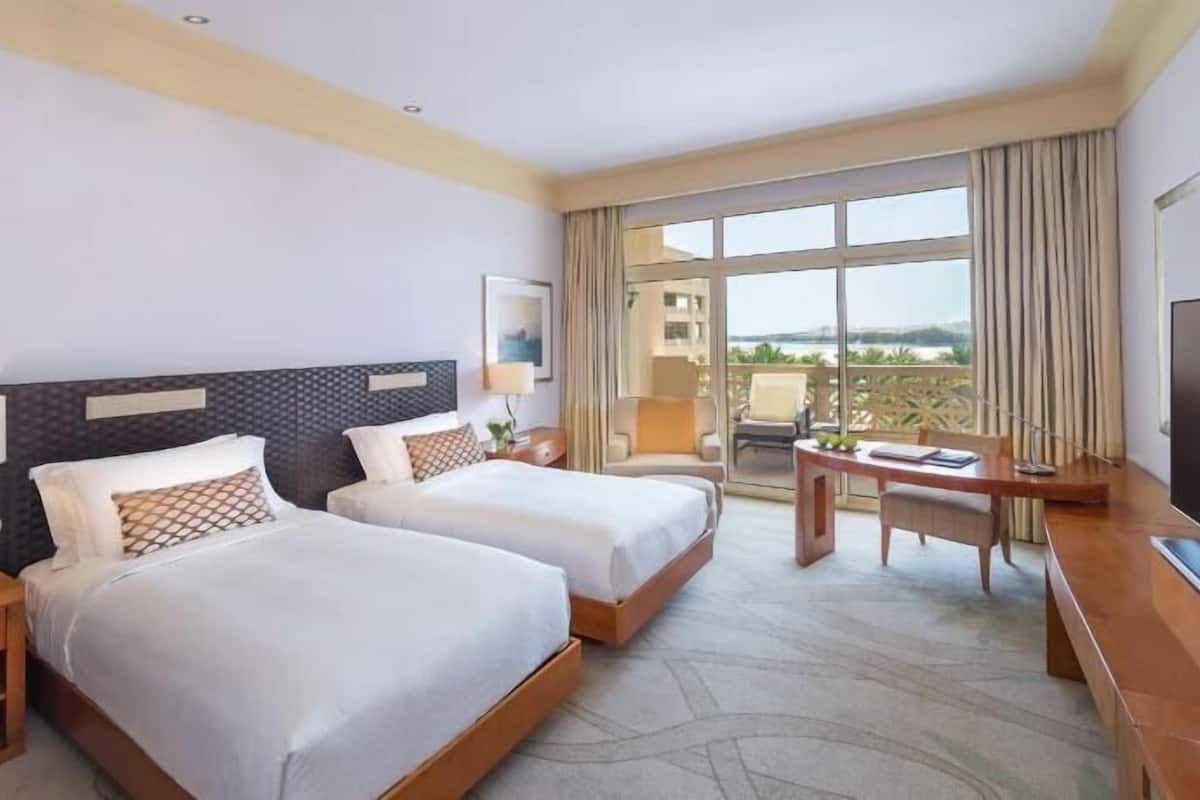 Quarto de hotel com duas camas, uma escrivaninha, televisão e varanda com vista.
