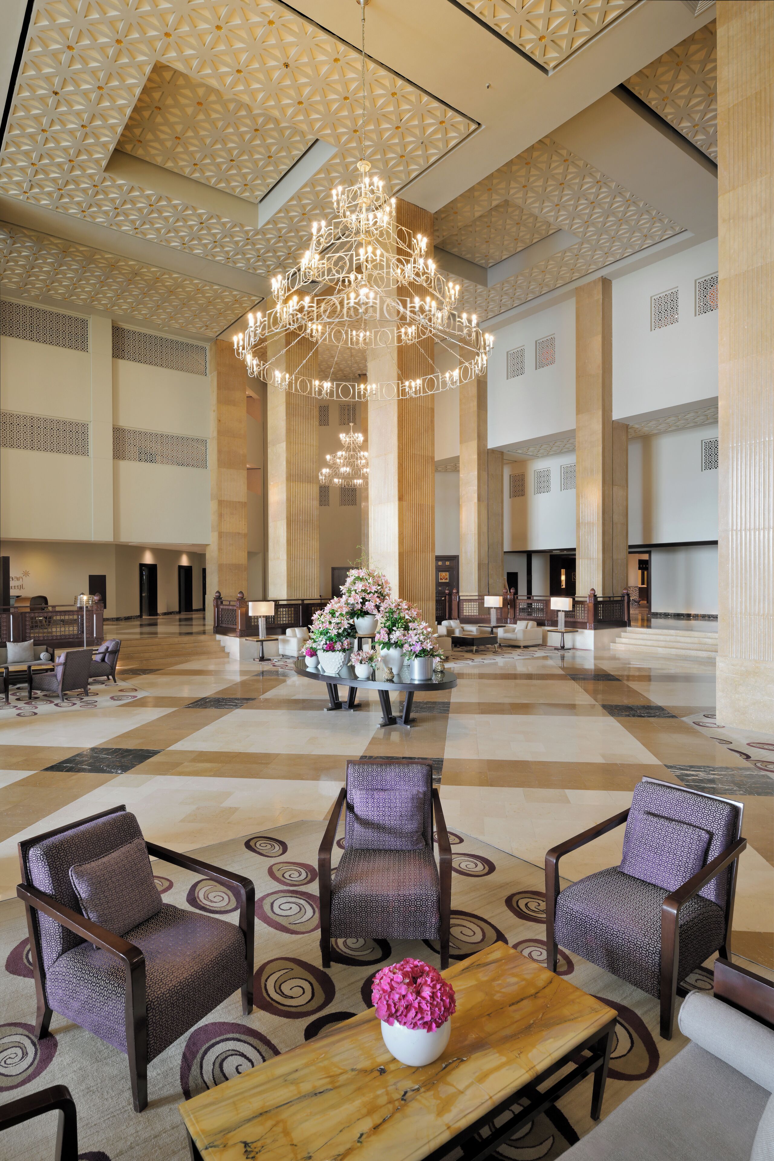 A spacious lobby with a large chandelier, seating area with armchairs and sofas, and a reception desk.