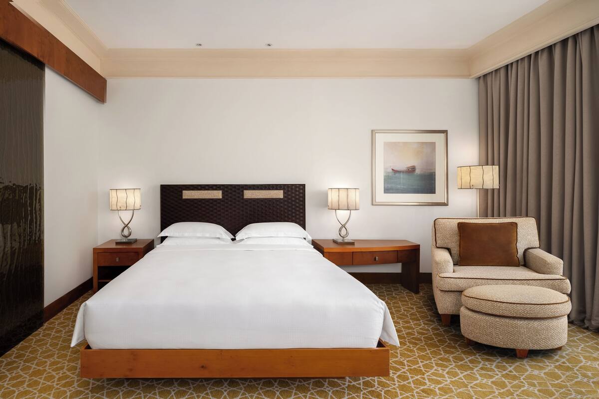 Quarto de hotel com uma cama grande, duas mesas de cabeceira, uma cadeira e um quadro na parede.