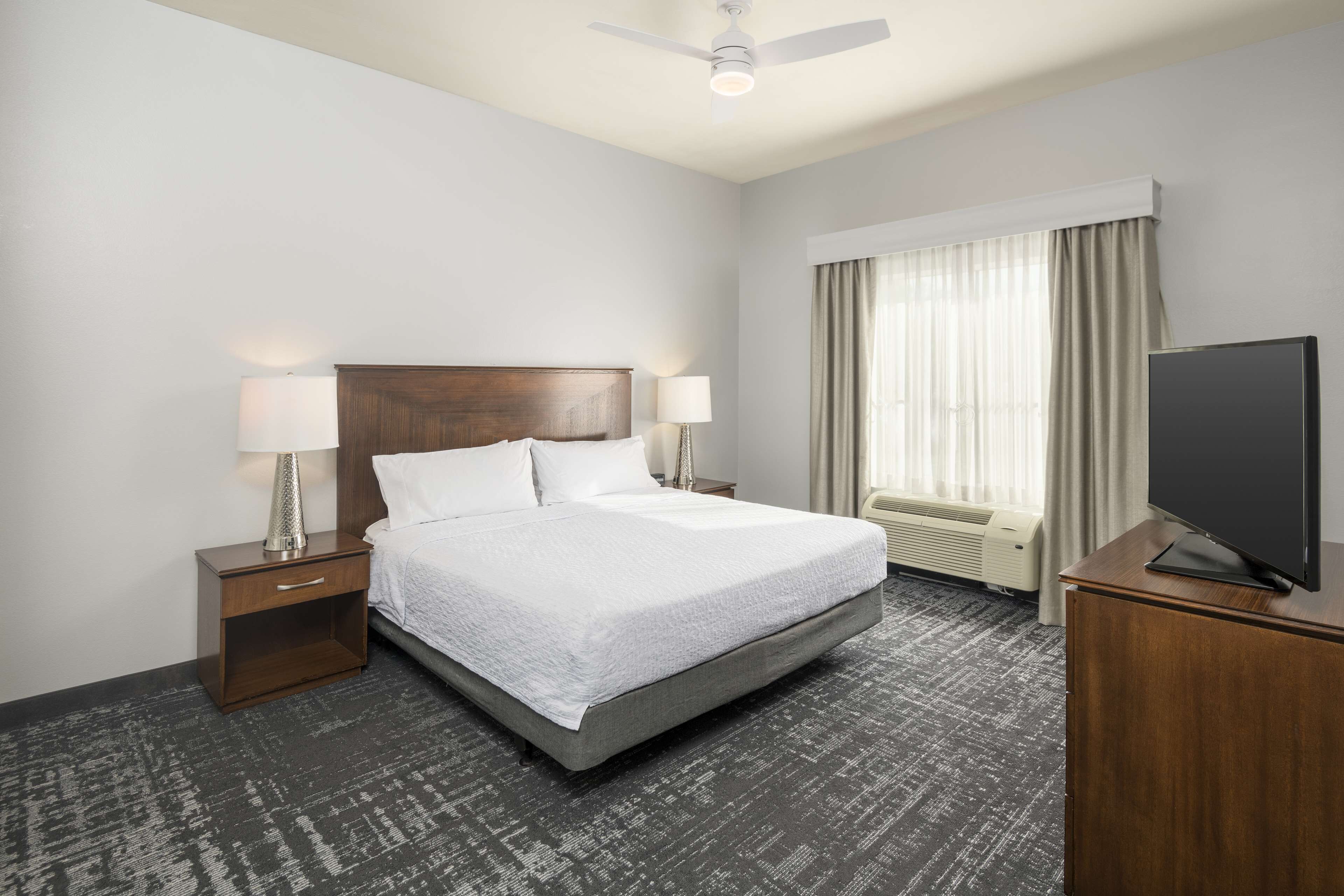 A hotel room with a bed, nightstands, a TV, and a window with curtains.