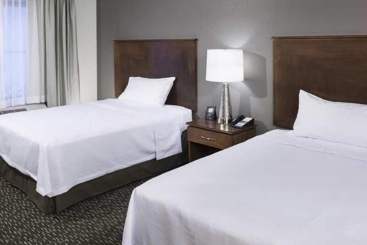Una habitación de hotel con dos camas, una mesita de noche con lámpara y una ventana con cortinas.
