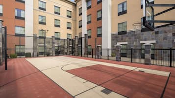 An outdoor basketball court adjacent to a multi-story building with a stone facade and a basketball hoop.