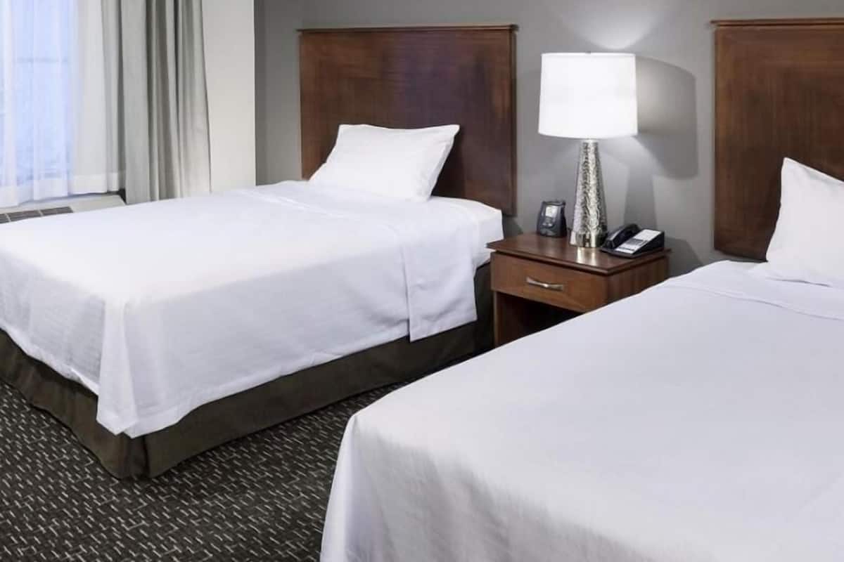 Una habitación de hotel con dos camas, una mesita de noche con lámpara y una ventana con cortinas.