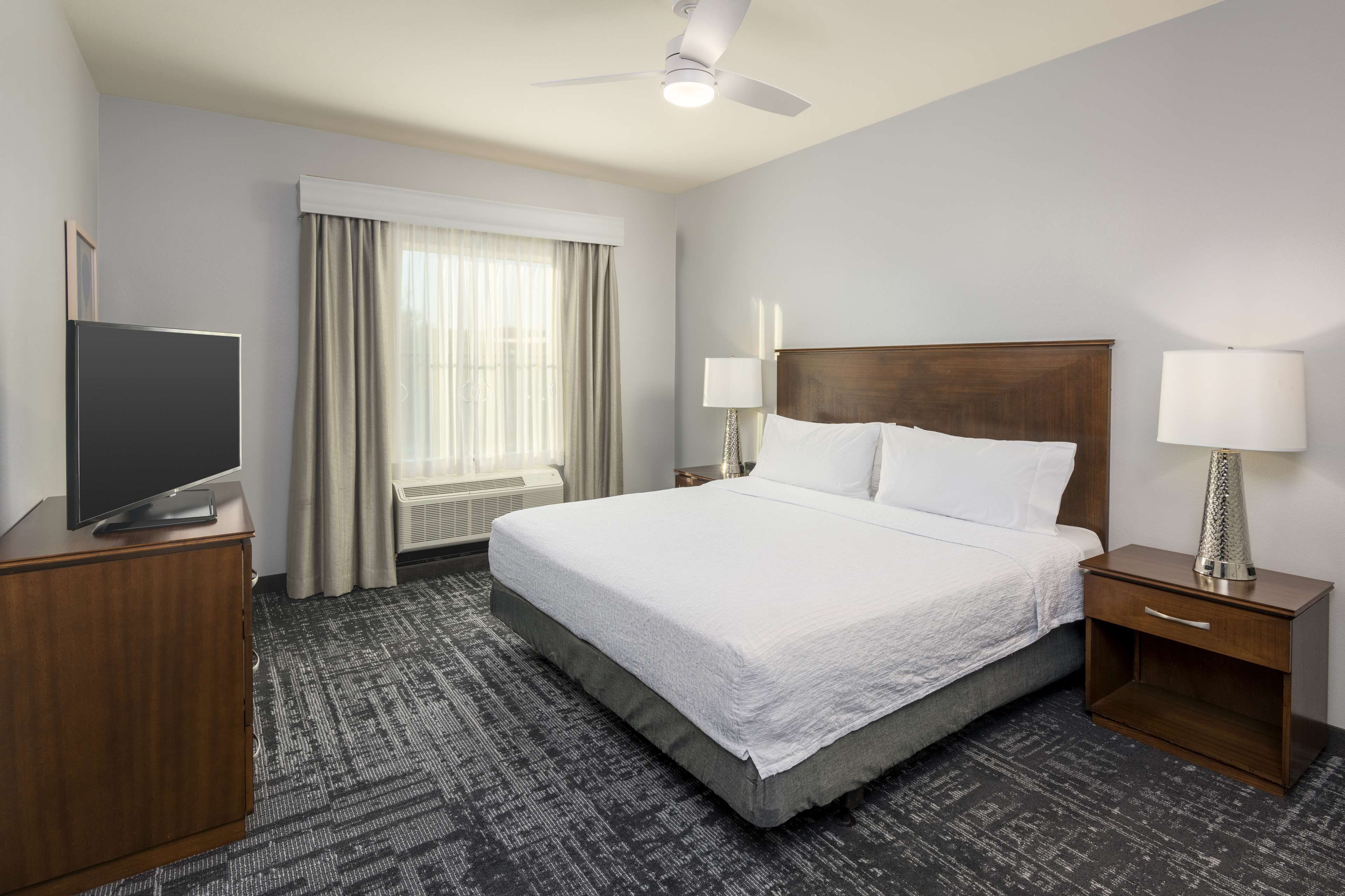 Habitación de hotel con cama, televisión, escritorio, lámpara y ventana con cortinas.