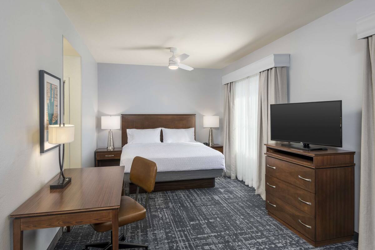 A hotel room with a bed, a desk, a chair, a television, and a dresser.