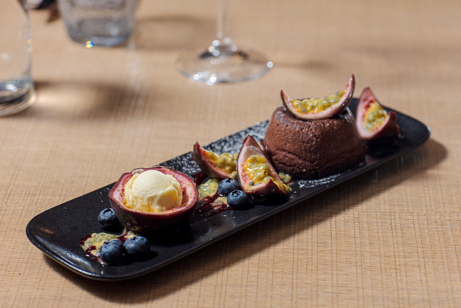 A dessert plate with a chocolate mousse, passion fruit halves, blueberries, and a scoop of ice cream.