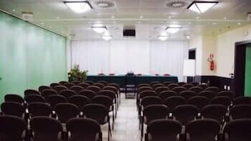 Una sala conferenze con file di sedie rivolte a un lungo tavolo coperto da una tovaglia verde.
