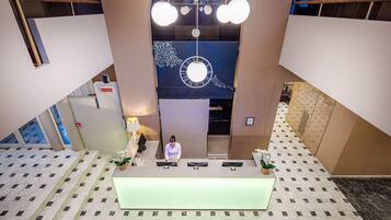 A hotel reception area with a central desk, a large clock, and a modern chandelier.