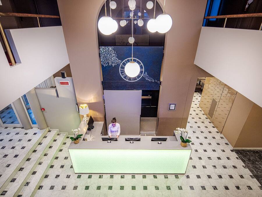 A hotel reception area with a central desk, a large clock, and a modern chandelier.