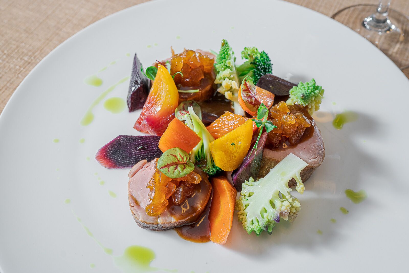 Une assiette blanche contenant une variété de légumes colorés et un morceau de viande, peut-être un steak, agrémenté de feuilles vertes.