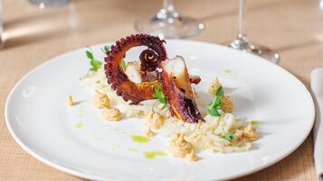 Une assiette de nourriture contenant un élément croustillant et enroulé, possiblement un légume ou de la viande, agrémenté d’herbes et de noix, le tout présenté sur une assiette blanche.