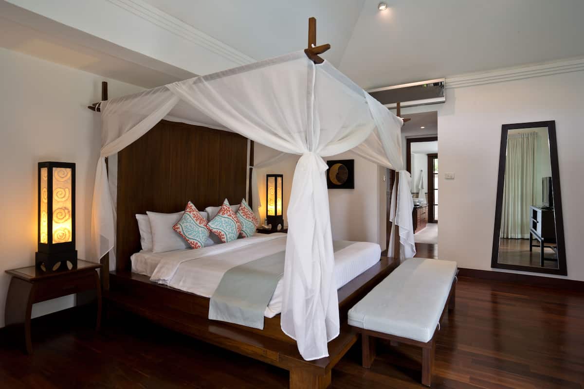 A four-poster canopy bed with a bench, bedside lamps, and decorative pillows.