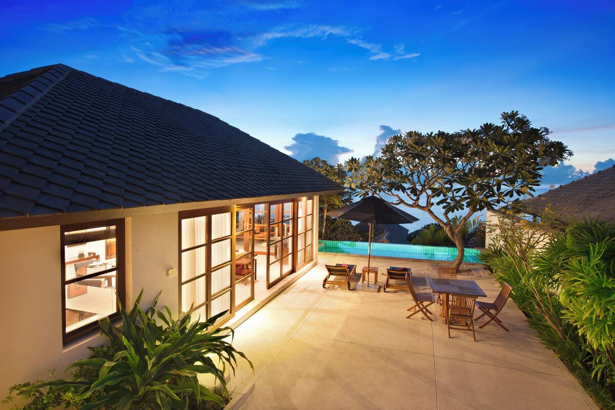 A house with a tiled roof, a large glass window, and a patio with outdoor furniture.